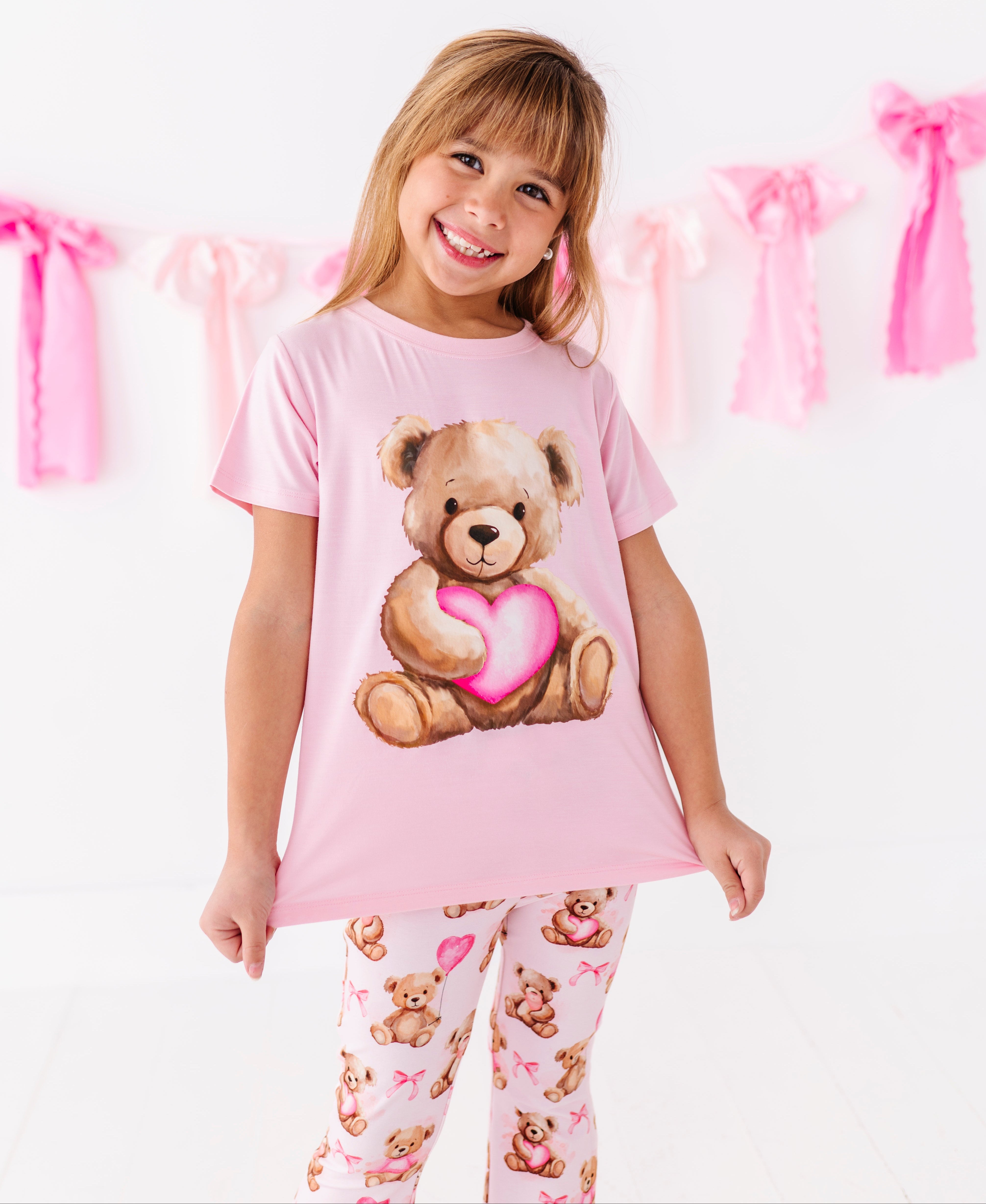 Toddler wearing pink bamboo graphic t-shirt featuring a teddy bear holding a heart